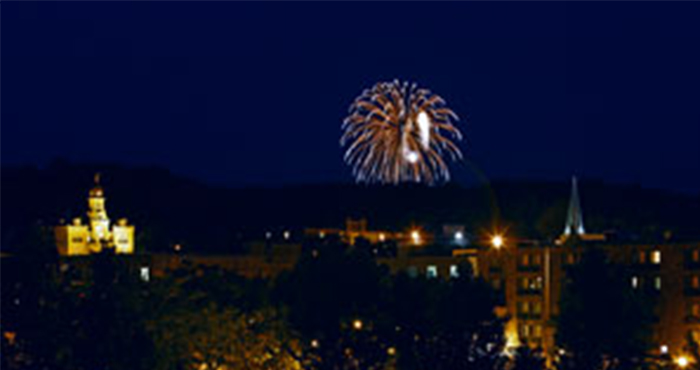 A tractor plows a sunlit field at dawn, creating dust while lush green crops flourish along the edge of the dirt path