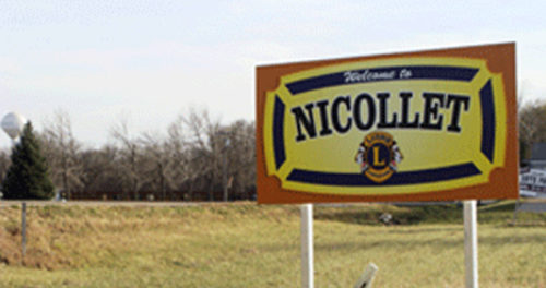 A tractor plows a sunlit field at dawn, creating dust while lush green crops flourish along the edge of the dirt path