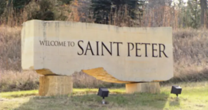 A tractor plows a sunlit field at dawn, creating dust while lush green crops flourish along the edge of the dirt path